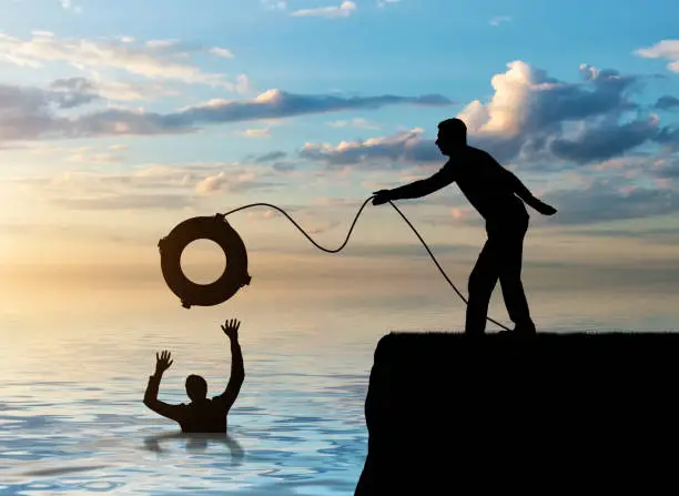 A silhouette of a man throws a lifeline to another man who is drowning in the water. The concept of mutual assistance in a business team