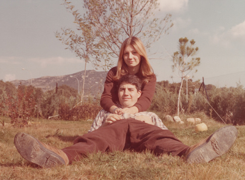 Image taken in the 70s: Smiling young couple lying on the grass looking at the camera