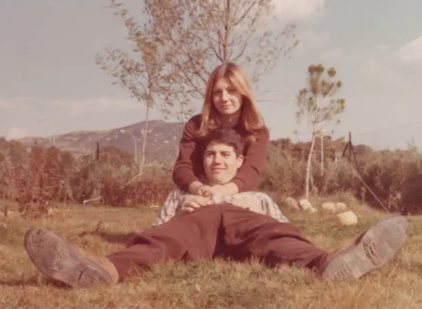 Photo of Image taken in the 70s: Smiling young couple lying on the grass looking at the camera