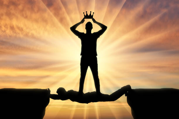 эгоистичный человек надевает корону на голову, он стоит на человеке в виде моста через пропасть - vanity стоковые фото и изображения