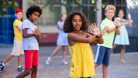 Positive african-american girl performing street dance with her friends outdoors.