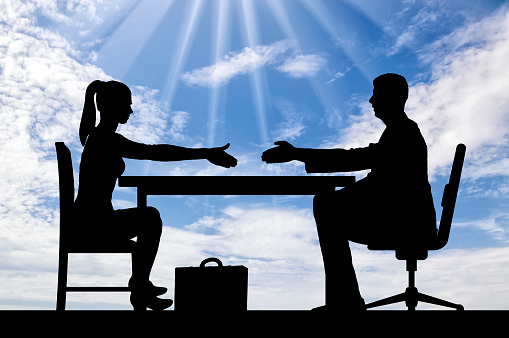 Silhouette of a man and a woman are sitting at a table and holding out each other's hands for a handshake. Concept hiring process