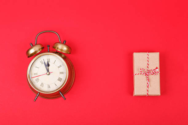 New Year's clock in gold color with a gift on a red background