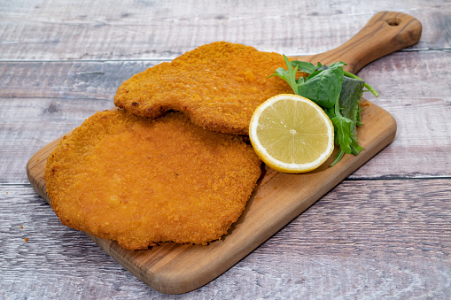 Two Wiener schnitzel placed on a serving board with lemon and garnish