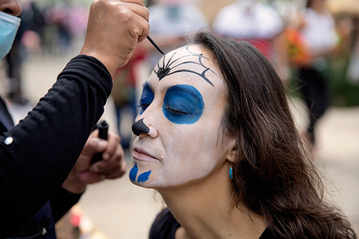 An attractive 40 something woman having her face painted at the annual Day of the Dead parade that takes place every year in late October in Mexico City every year.\nDía de los Muertos, or Day of the Dead, is one of Mexico's most recognized holidays. The celebration from Oct. 31 to Nov. 2 commemorates death as an essential element of life and honours loved ones who have passed away.