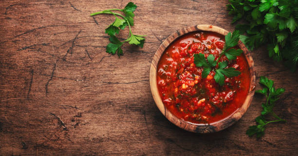 Caucasian cuisine. Traditional armenian hot adjika sauce with hot pepper, paprika, garlic and parsley on rustic wood kitchen table background, top view banner stock photo