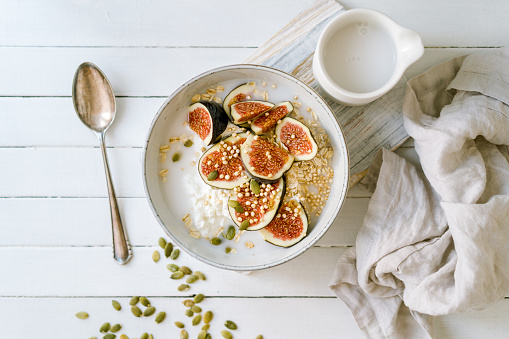 Sliced figs, oats and quinoa with pumpkin seeds and a coconut drink in a bowl