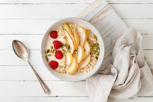 Raspberries, oats and a sliced pear together with soy yogurt in a bowl