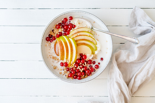 Red currants, granola and a sliced pear with oatmeal and curd cheese in a bowl