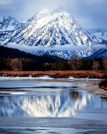 A snow mountain in the background reflects in the icy lake in the foreground