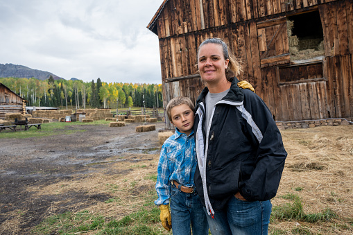 Young Mother and Son Posing in front of Their Rustic Barn and Homestead in the Autumn Under a Dramatic Cloudscape in Southwestern Colorado Near Wilson Peak and Telluride