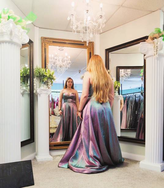 Teenager Trying On Prom Dress A beautiful teenage girl with long blonde hair, is wearing a prom dress and is looking at herself in the mirrors of the dress shop. prom dress stock pictures, royalty-free photos & images