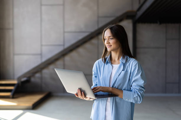 istock Portrait of smiling woman using laptop while standing at home 1438749741