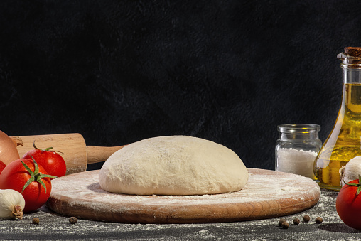 Dough and ingredients for making pizza on a black background.