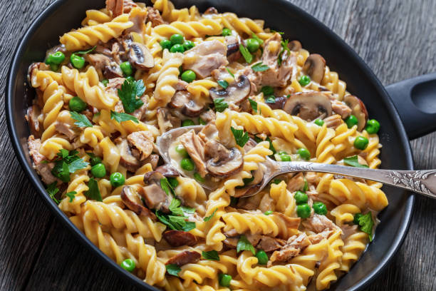 tuna mushroom green pea fusilli with creamy cheese sauce in pan on dark wood table, close-up