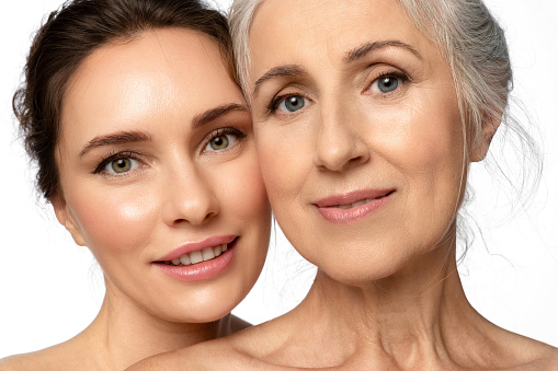 Two generations of beautiful women, mother and daughter, hugging sweetly and looking. Close-up portrait about caring for different facial skin types and good intergenerational relationships.