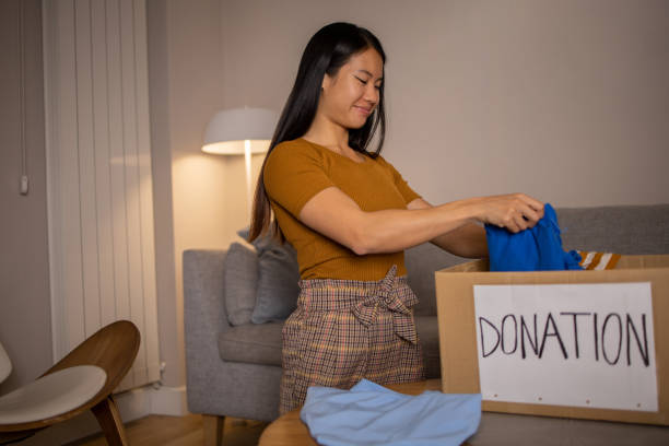 istock Young woman sorting clothing and packing donation box 1438758992