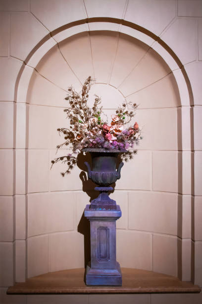 Urn filled with dried flower arrangement sitting on pedestal inside curved alcove or niche in stone wall - very formal Urn filled with dried flower arrangement sitting on pedestal inside curved alcove or niche in stone wall - very formal alcove stock pictures, royalty-free photos & images