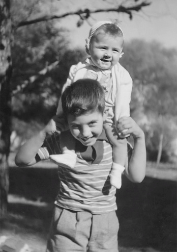 Imagen en blanco y negro tomada en los años 50: niño cargando a su hermana pequeña sobre sus hombros photo