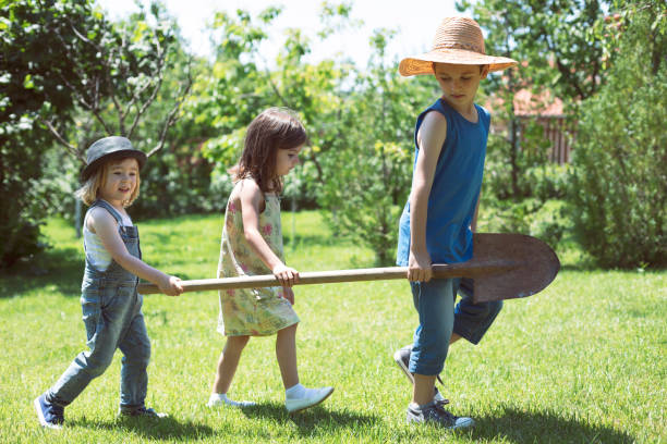 Three small children carrying old rusty shovel