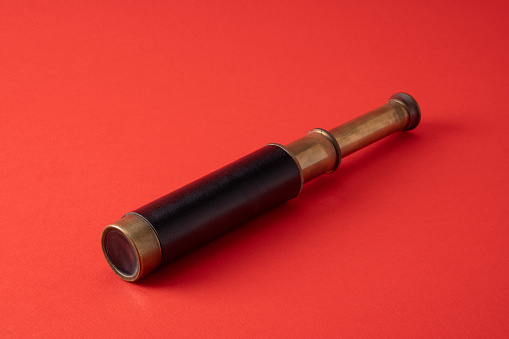 Close up photo of old fashioned hand held telescope on red background. No people are seen in frame. Shot in studio.