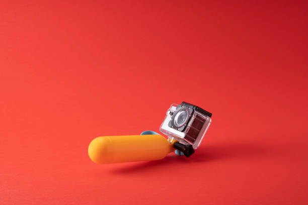 Close up photo of wearable action camera on red background. No people are seen in frame.  The camera is in underwater shield. and is attached to floating device. Shot with a full frame mirrorless camera.