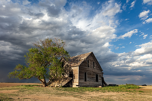 An old, abandoned house with a lone tree and dark storm clouds in rural Nebraska.