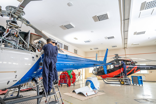Aircraft mechanics standing on ladder and repairing propeller engine, back view view. Engineers team working in airplane hangar, wide shot
