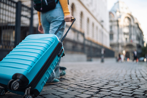 Rear view of young female tourist walking in the city with suitcase.