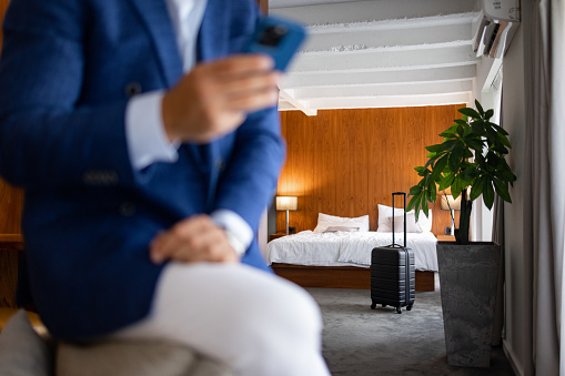 Businessman texting and using mobile phone with focus on hotel bed