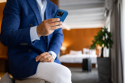 Business man texting on the phone in the hotel room and wearing navy blue smart coat