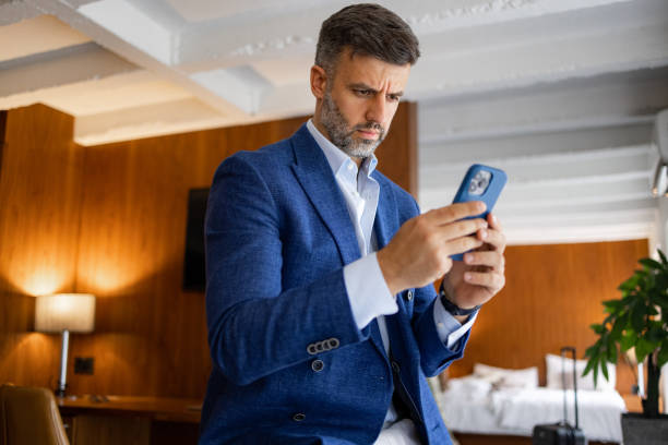 istock Elegant handsome man using mobile phone in his hotel room, while on a business journey 1438774463