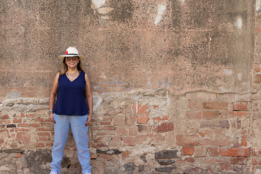 Brunette Latina with hat, leaning against a wall of an abandoned hacienda, posing