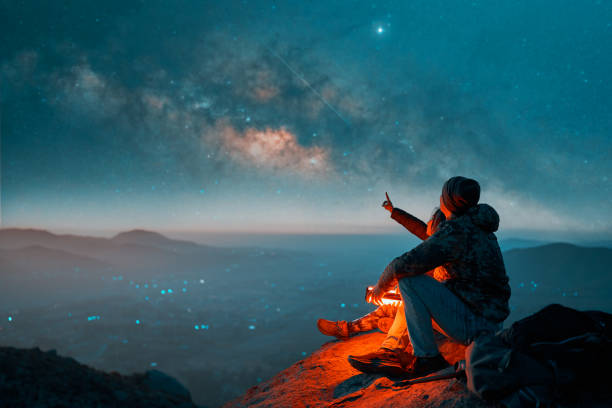 siluetas de una pareja latina sentada en la cima de la colina mirando estrellas fugaces y la vía láctea en el fondo - natural looking fotografías e imágenes de stock