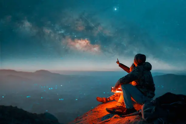 Photo of silhouettes of a latin couple sitting on the top of the hill looking at shooting stars and the milky way in the background