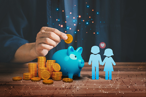 Man hand putting golden money coin into blue piggy bank for saving money, concept of saving to wedding, travel, buy a house, real estate or home, finance and investment.