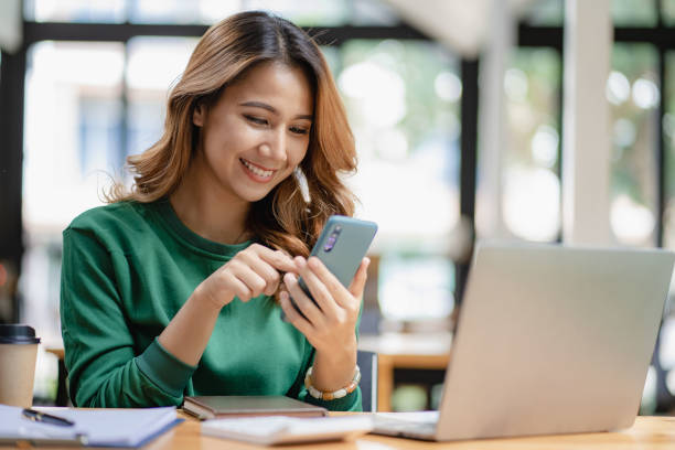 istock Asian woman talking on smartphone, working from home, digital phone technology lifestyle work from home with laptop financial concept 1438792451