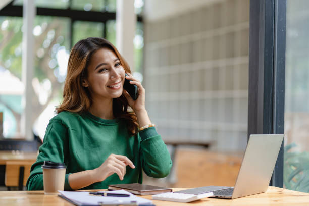 istock Asian woman talking on smartphone, working from home, digital phone technology lifestyle work from home with laptop financial concept 1438792457