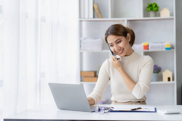 istock Asian woman talking on smartphone, working from home, digital phone technology lifestyle work from home with laptop financial concept 1438792651