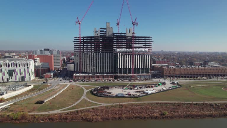 Drone shot of construction workers and tall cranes building large structure near university campus in United States Midwest city