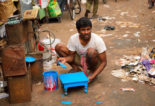 Kolkata, India - March 26, 2017: A worker painting a stool blue by the street side.