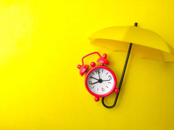 istock A red alarm clock with yellow umbrella on a yellow background with copy space. 1438802176