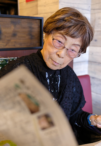 A senior woman reading a newspaper curiously.