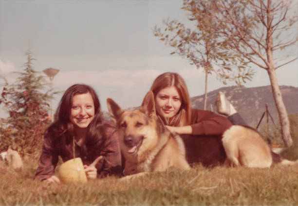 Image taken in the 70s: Smiling Young lesbian women posing with their dog sitting on the ground stock photo