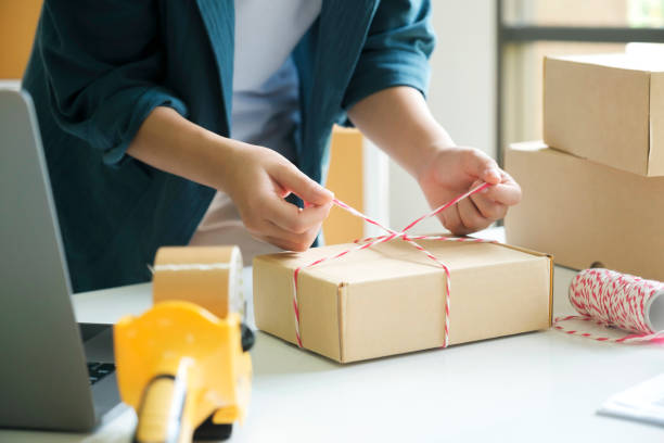 Woman packing parcel and tying with rope for shipping. stock photo