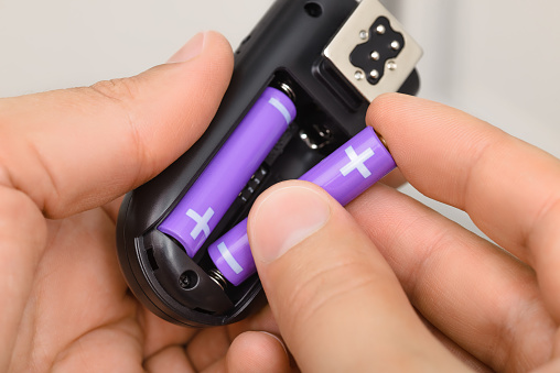 Hands replacing purple AAA alkaline battery in the black electronic device.