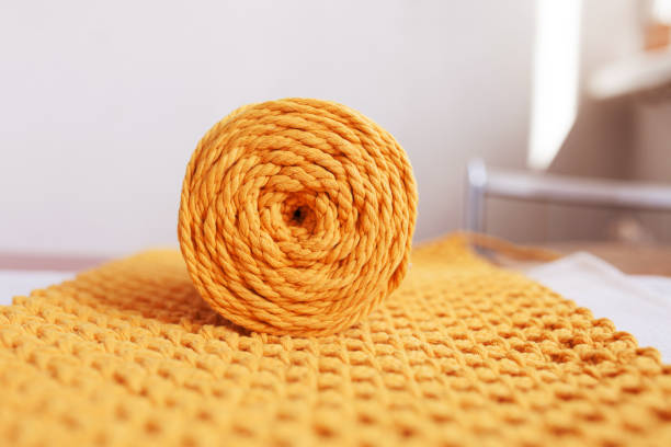 Handmade macrame braiding and cotton threads on ornate background. Yellow cotton macrame cord and rope. Good image for macrame and handicrafts banners and advertisement.  Female hobby. Close up. stock photo