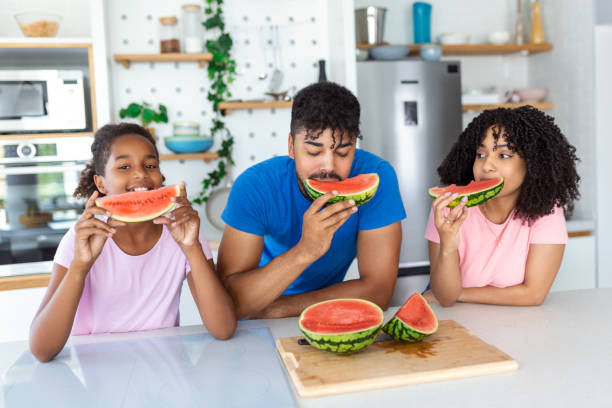 Family eats a sweet watermelon in the kitchen. A man and a woman with daughter eat a ripe watermelon in the kitchen. Happy family eating watermelon.