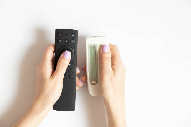 istock Two remote controls in female hands on a white background close-up, TV 1438844039