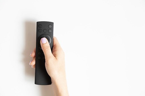 Remote control in a female hand on a white background close-up, TV remote control